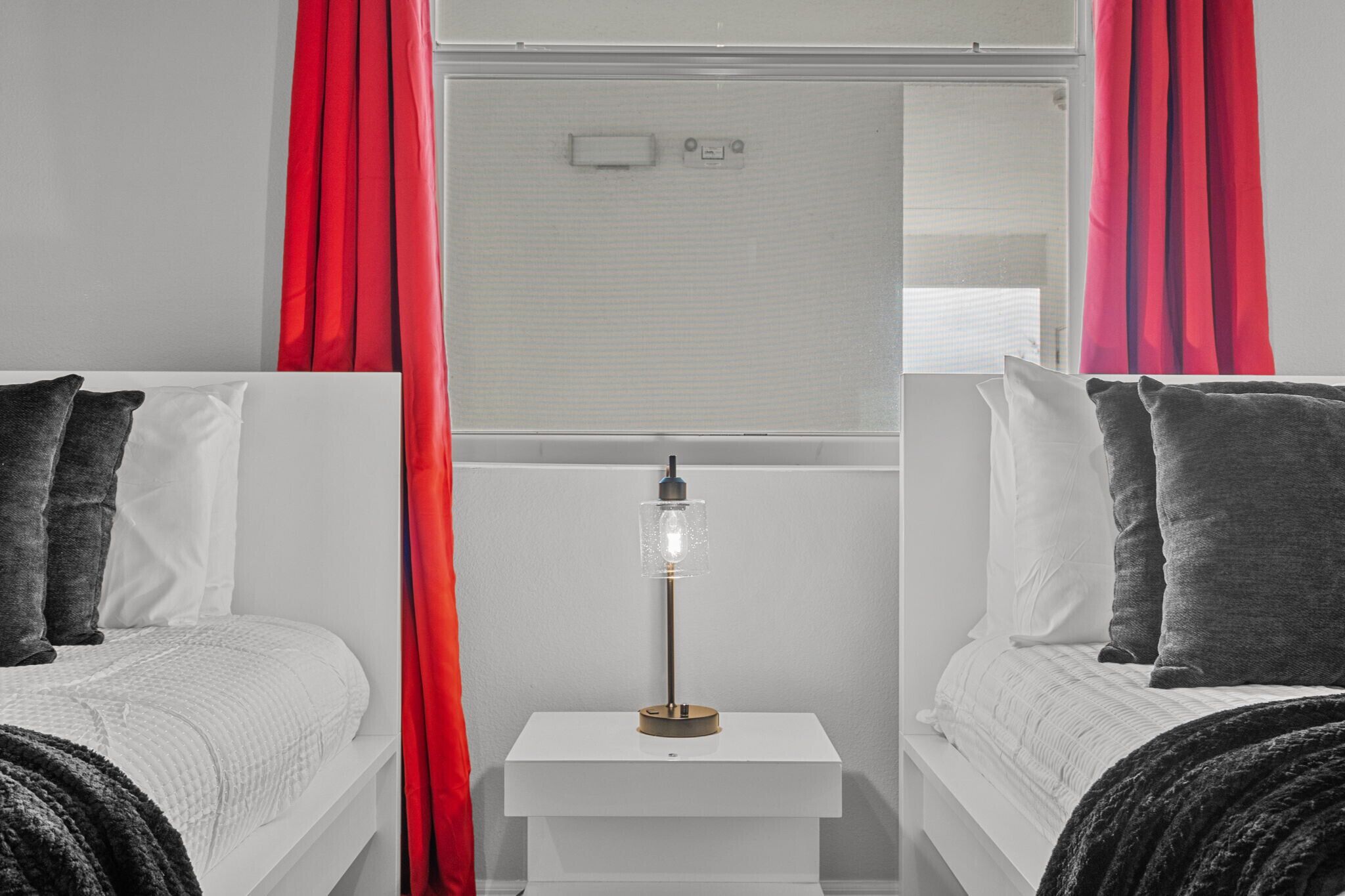 Camera da letto con due letti, un comodino, una lampada e tende rosse.