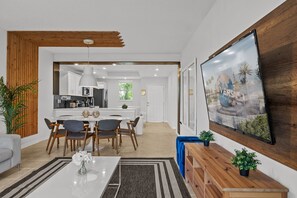 Eine moderne Küche mit weißen Schränken, einer zentralen Kochinsel und einem Essbereich mit weißem Tisch und Stühlen.