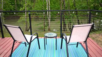 A deck with two chairs and a small table, overlooking a river and forest.