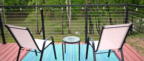 Une terrasse avec deux chaises et une petite table, donnant sur une rivière et une forêt.
