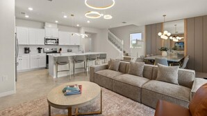 Una cocina moderna con armarios blancos, una isla central con taburetes y un comedor con mesa de vidrio y sillas.