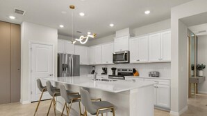 Una cocina moderna con armarios blancos, una isla central con taburetes de bar, electrodomésticos de acero inoxidable e iluminación empotrada.