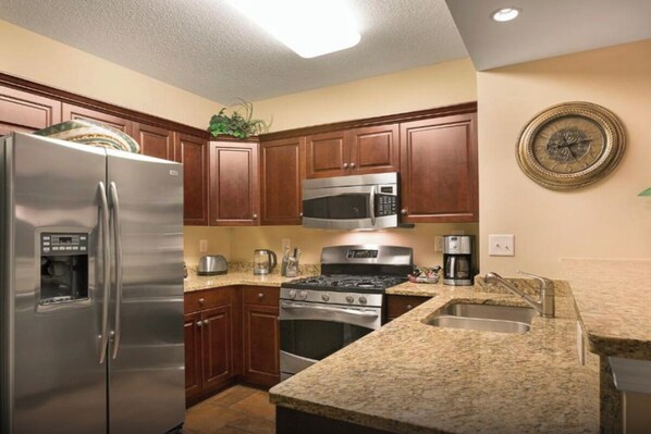 A kitchen with wooden cabinets, stainless steel appliances, granite countertops, and a clock on the wall. - Beachfront Condo | Pools & Swim-Up Bar | Near Golf & Shops (North Myrtle Beach)