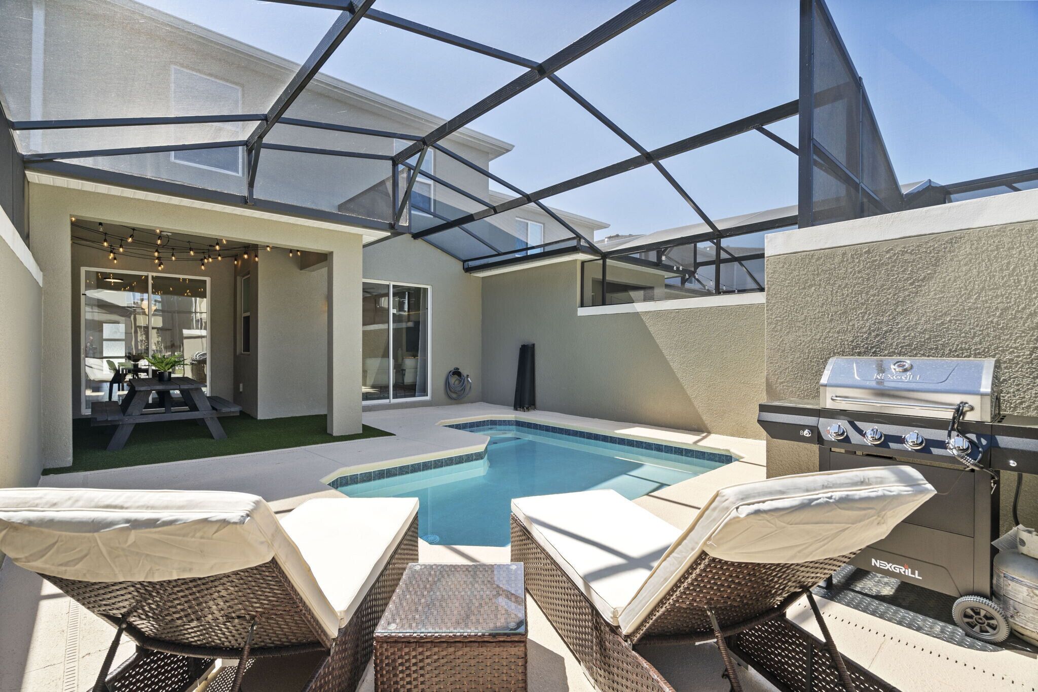 A backyard with a swimming pool, outdoor seating, a grill, and a covered patio area.