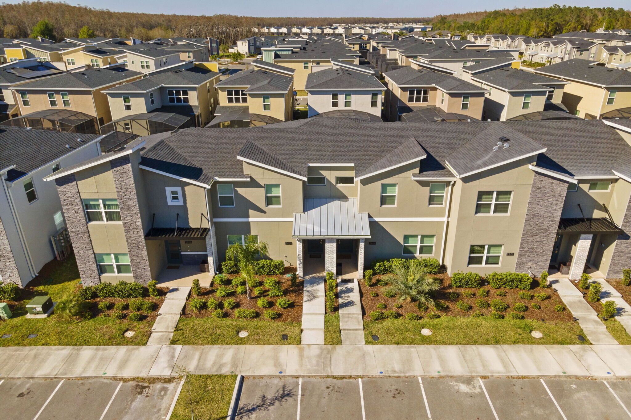 A residential complex with multiple two-story houses, a central entrance with a covered walkway, and a parking area in front.