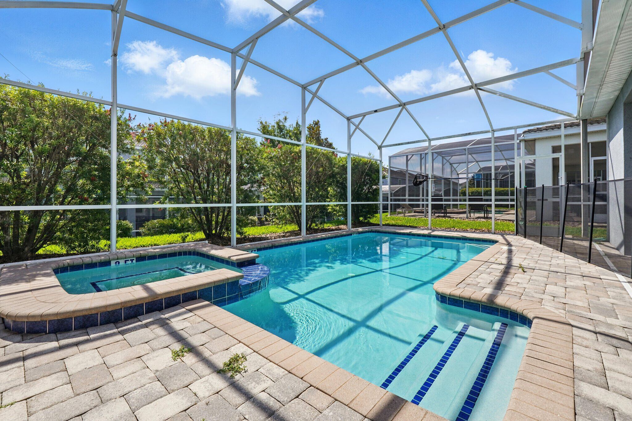 Ein überdachter Außenpool mit Whirlpool, umgeben von einer Ziegelterrasse und üppiger Bepflanzung.