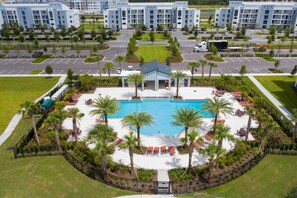 A hotel with a central swimming pool surrounded by palm trees and sun loungers, with a parking lot and a road in the background. - Last Minute Disney Getaway! Luxury Condo with Private Balcony. Book Now! #154617 (Orlando)
