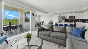 Ein modernes Wohnzimmer mit einem grauen Sofa, einem Glastisch und Blick auf einen Balkon.