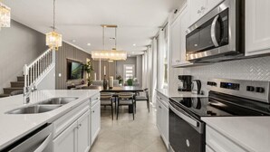 A modern kitchen with white cabinetry, stainless steel appliances, and a dining area with a table and chairs. - Last Minute Disney Getaway! Private Pool & Themed Bedrooms. Book Now! #150497 (Orlando)