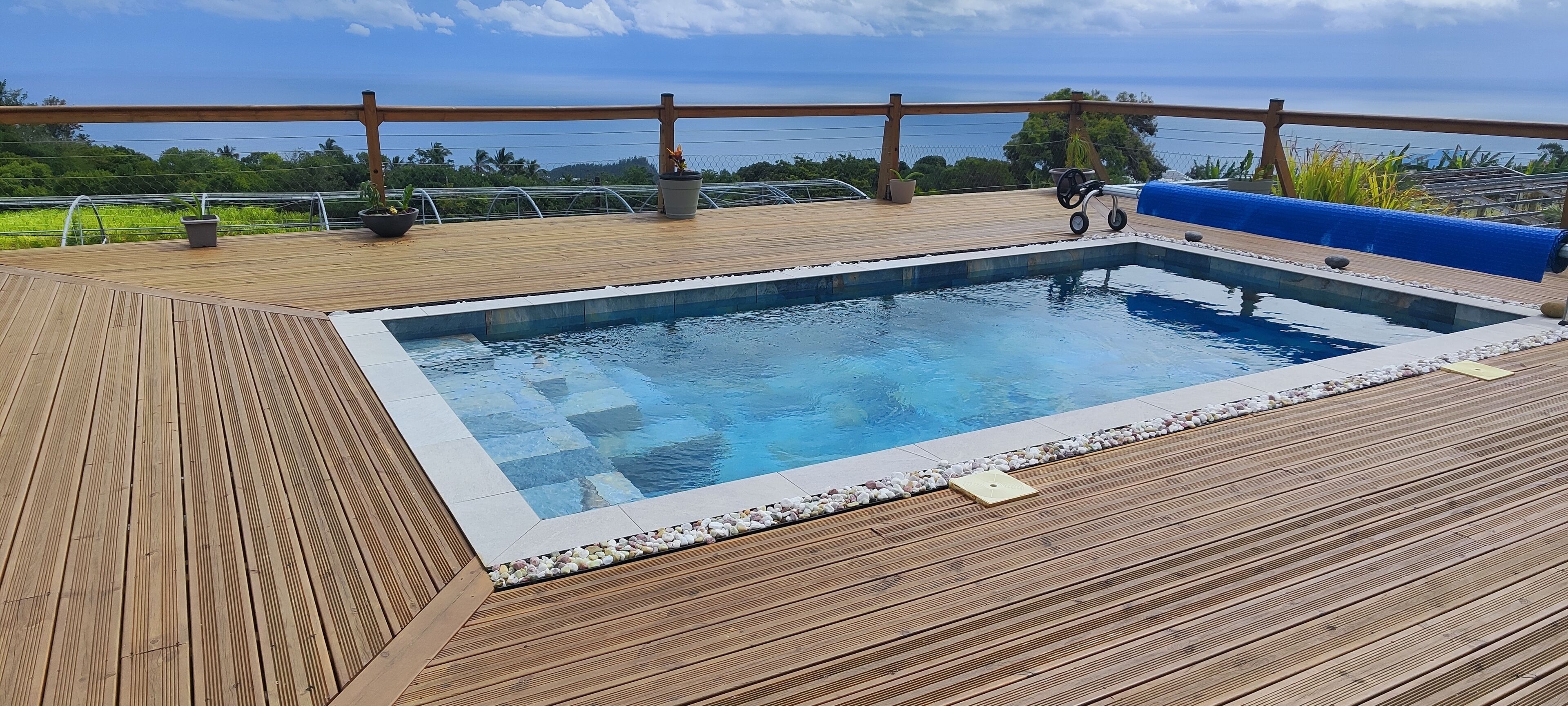 En træterrasse med swimmingpool, omkranset af et trægelænder og krukker med planter.