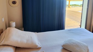 A hotel room with a bed, two decorative wall hangings, a window with a view of the beach, and a curtain. - Beautiful contemporary villa on one level, swimming pool, ideal for a stay in Reunion Island (Petite-Île)