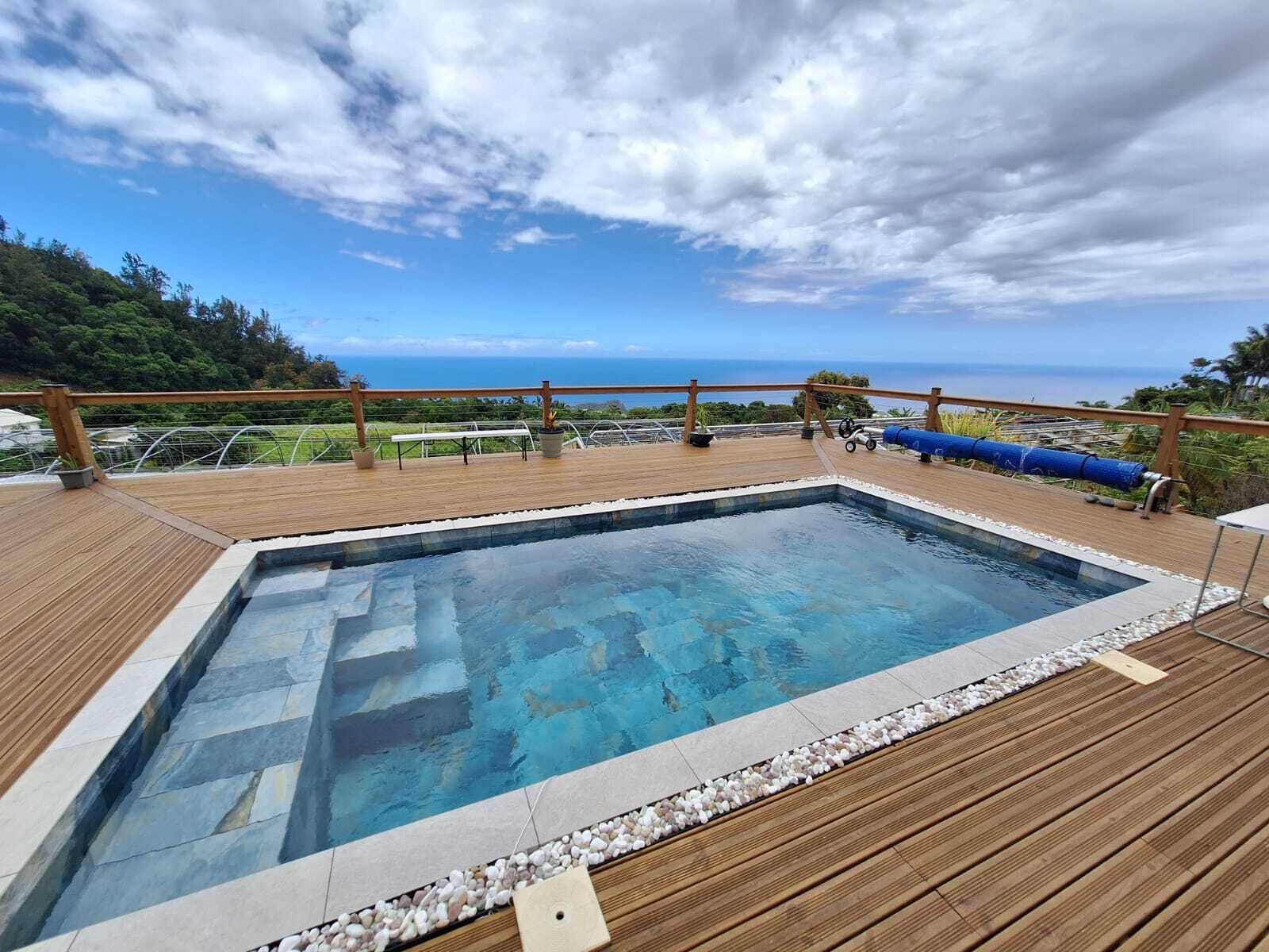 Terraza de madera con piscina, rodeada por una barandilla, con vistas panorámicas.