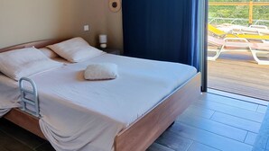 A bedroom with a bed, a ceiling fan, a nightstand, and a view of an outdoor area with chairs. - Beautiful contemporary villa on one level, swimming pool, ideal for a stay in Reunion Island (Petite-Île)