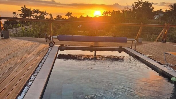 A rectangular pool with a wooden deck and stone tiles, surrounded by a wooden fence, with a sunset in the background. - Beautiful contemporary villa on one level, swimming pool, ideal for a stay in Reunion Island (Petite-Île)