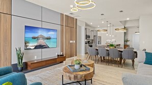 A modern living room with a large flat-screen TV, wooden accents, and a dining area with grey chairs. - Last Minute Disney! Private Pool, Hot Tub, Game Room & Themed Bedrooms. Book Now! #150825 (Orlando)