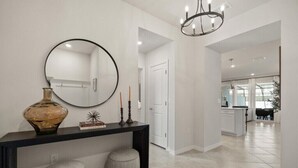 Un interno moderno con una consolle, due pouf, uno specchio rotondo e un lampadario.