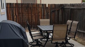 Un patio exterior con una parrilla cubierta, una mesa y cuatro sillas.