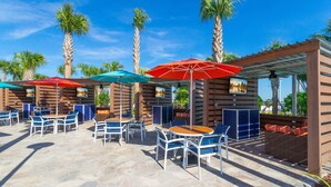 Un espace extérieur aménagé en terrasse, avec un sol en pierre, des tables, des chaises et des parasols.