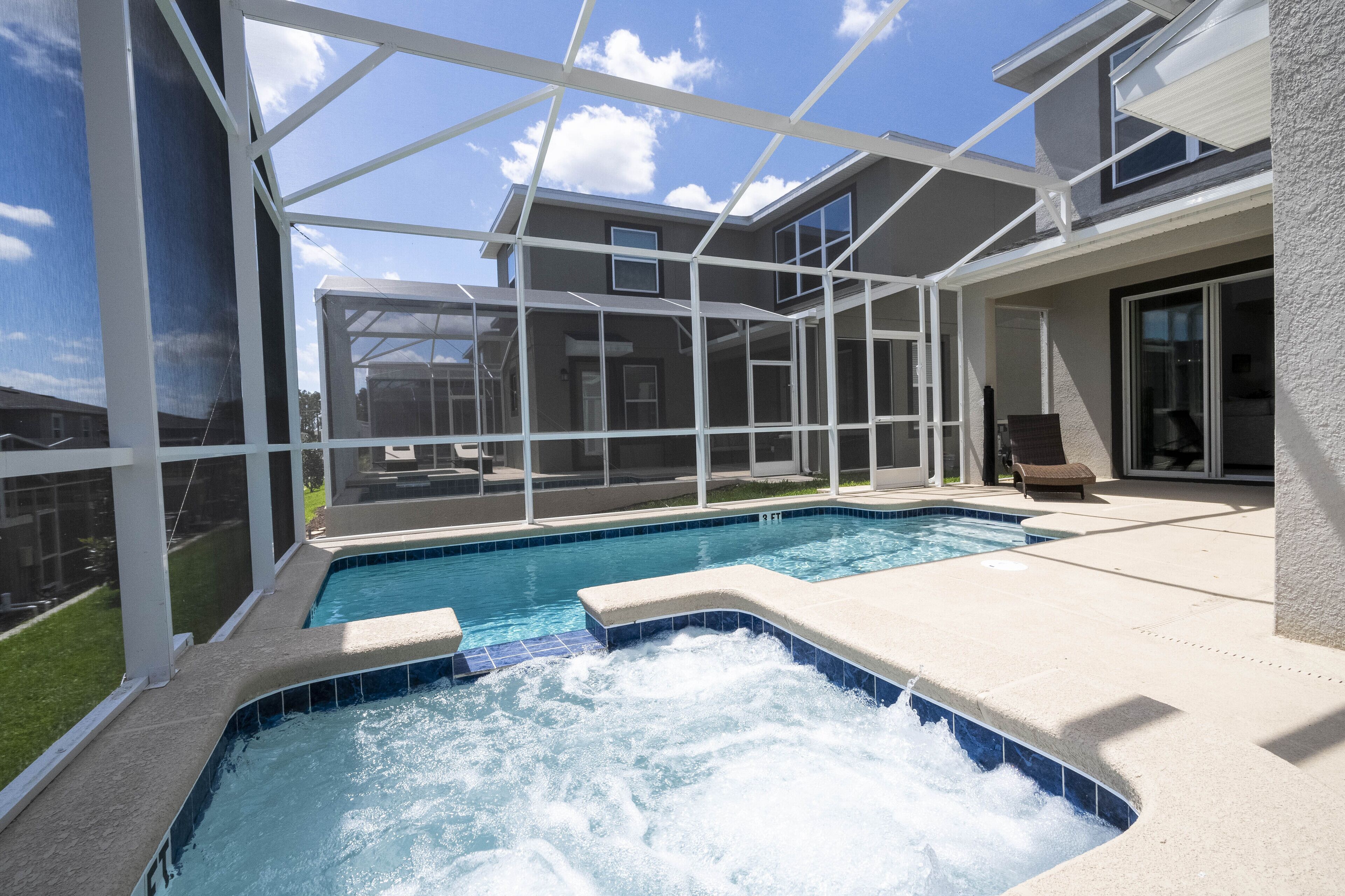 A swimming pool with a hot tub, surrounded by a covered patio with a view of a house.