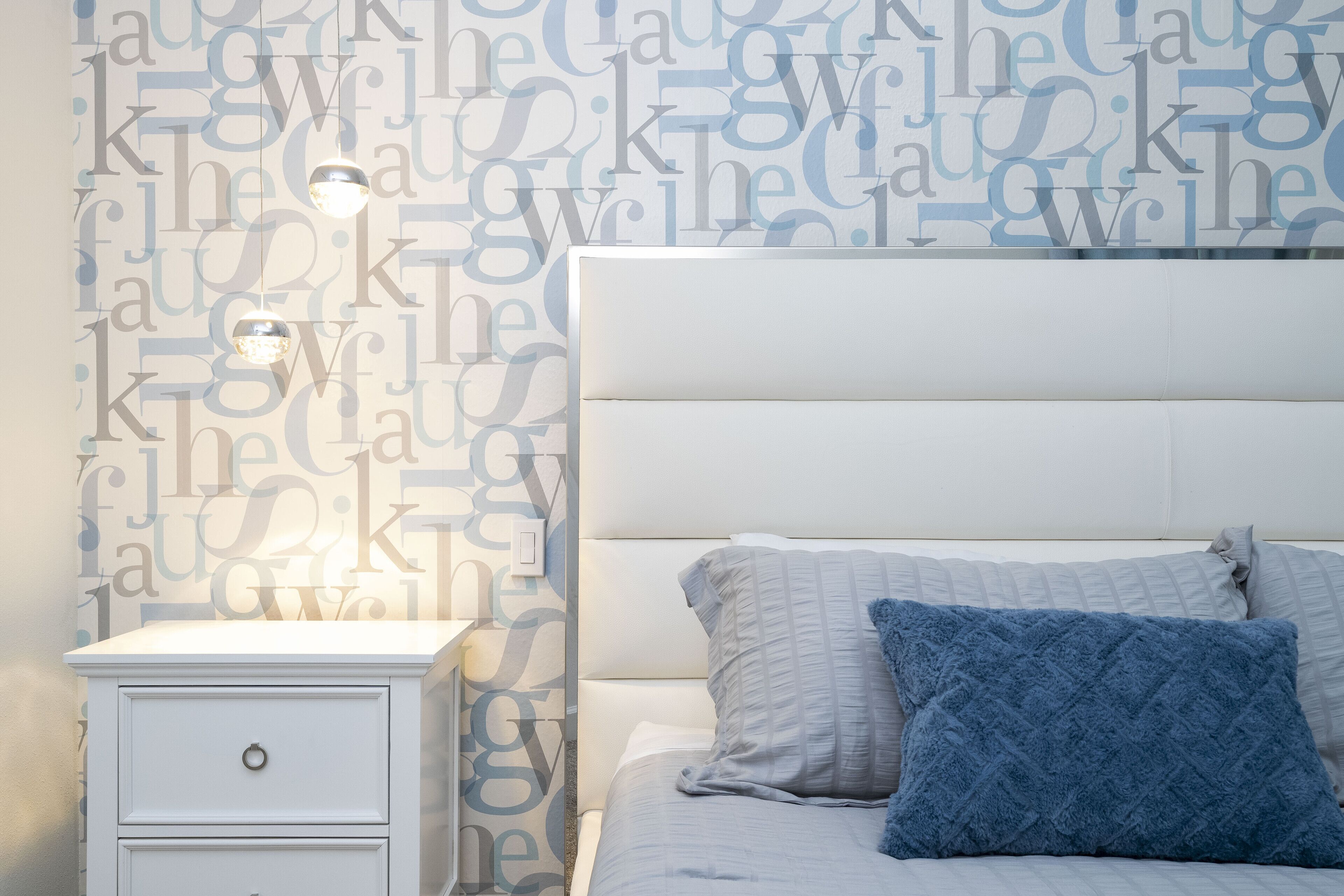 Une chambre avec une table de chevet blanche, un lit doté d’une tête de lit et un mur orné d’un motif répétitif.