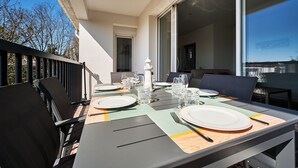 Mesa con platos, cubiertos, vasos y una jarra de agua en un balcón con sillas y vistas al cielo.