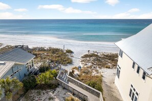 A beach view with a wooden boardwalk leading to a building with a metal roof. - The Lumina (Santa Rosa Beach)