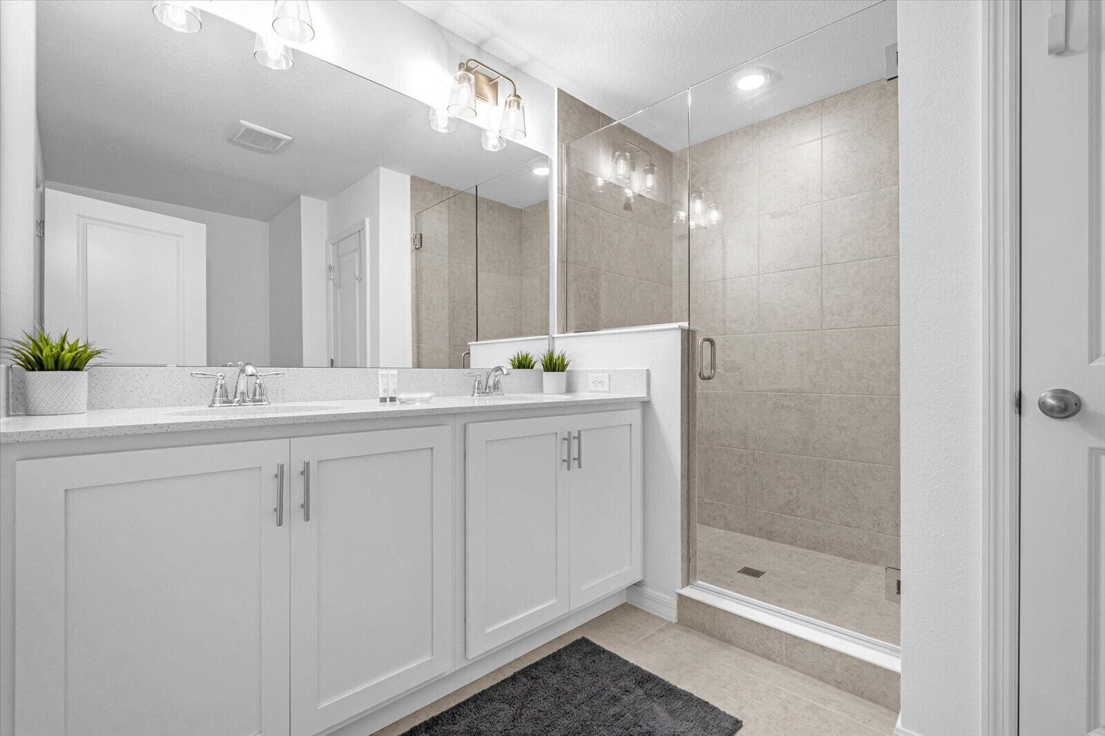 Un baño moderno con un espejo grande, dos lavamanos, una ducha y una alfombra oscura.