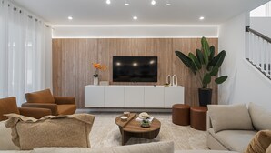 Un salon moderne doté d’un téléviseur à écran plat, de murs recouverts de panneaux en bois, d’une grande plante et d’un escalier.