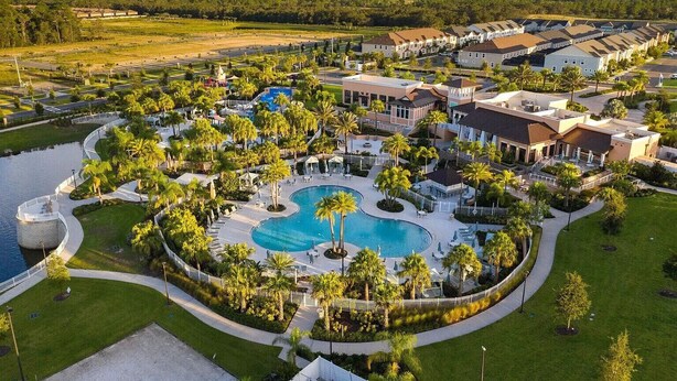 Vue aérienne d’un complexe hôtelier doté d’une piscine centrale, entouré de palmiers et de différents bâtiments.