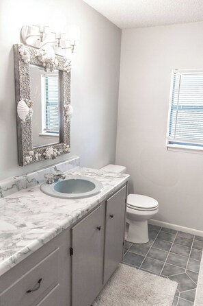A bathroom with a marble sink, a toilet, and a window with blinds. - 3BR Emerald Escape /Steps from Beach (Panama City Beach)