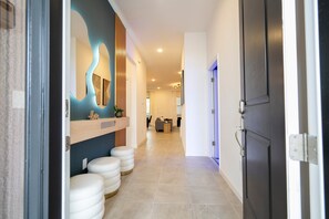 A hallway with a modern design, including a wooden accent wall, a mirror, and a seating area with white stools. - Last Minute Disney! Private Pool, Hot Tub, Game Room & Themed Bedrooms. Book Now! #127375 (Orlando)