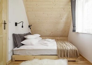 A small, cozy bedroom with a wooden sloped ceiling, a bed with white bedding, a fluffy white rug, and a window with sheer curtains. - Highlander Holiday Home With a Fireplace, Zakopane (Zakopane)