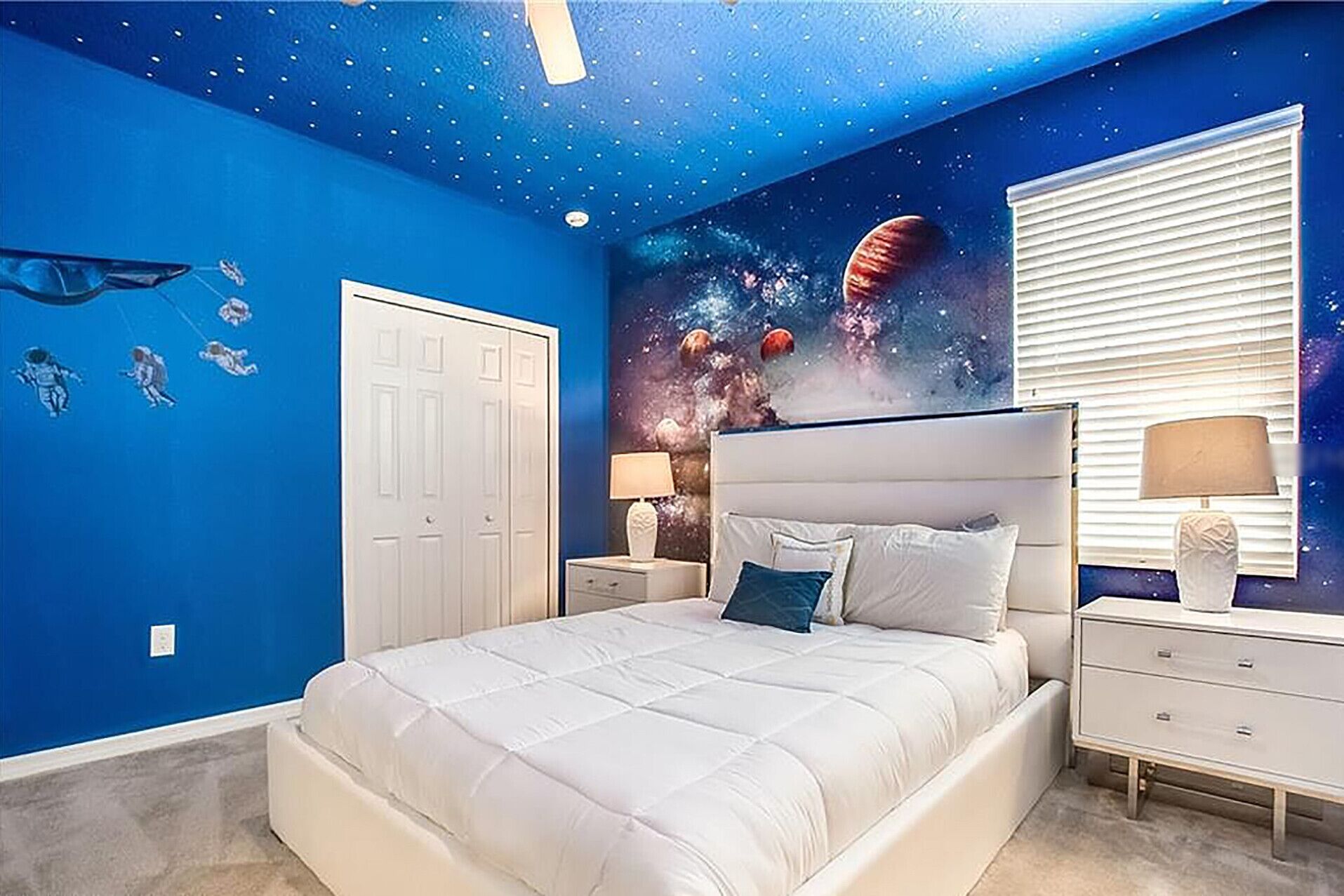 A bedroom with a bed, nightstands, a dresser, a starry ceiling, and a space-themed wall mural.