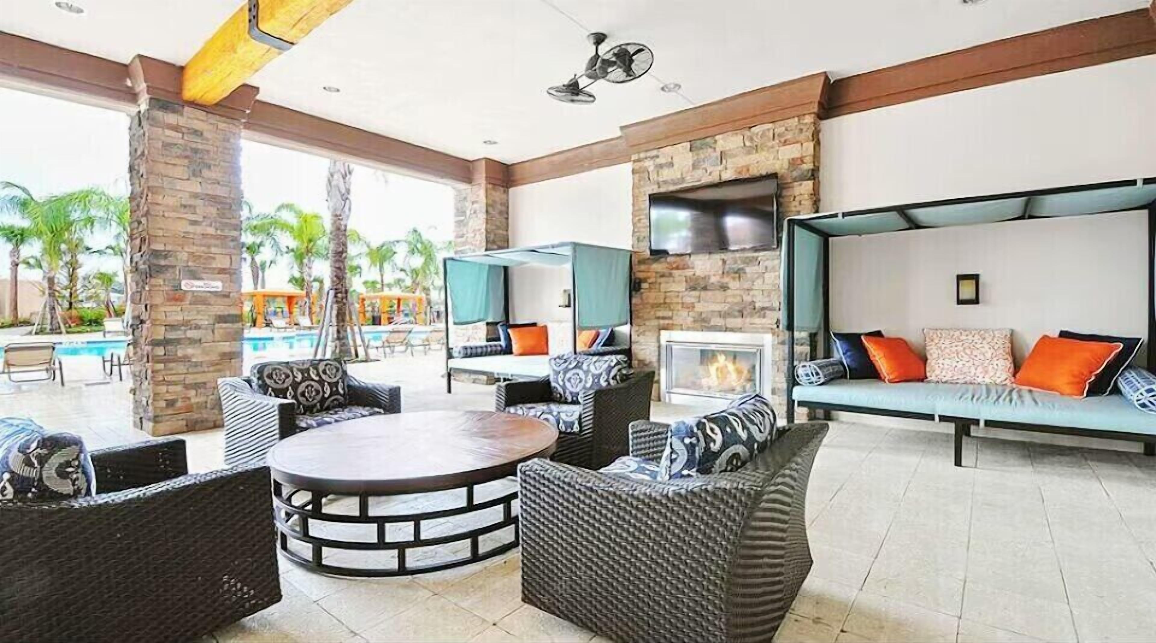 A spacious outdoor lounge area with wicker furniture, a round table, and a TV mounted on a stone wall.