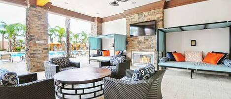 A spacious outdoor lounge area with wicker furniture, a round table, and a TV mounted on a stone wall.
