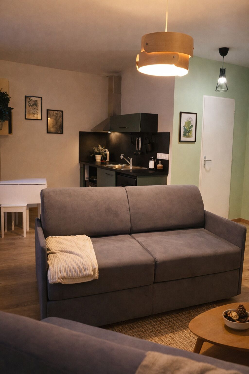 A living room with a grey sofa, a small round table, and a kitchen area in the background.