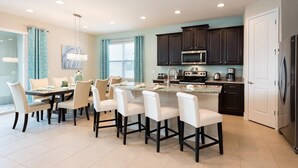 Una cocina moderna con armarios oscuros, una isla central con taburetes de bar, un microondas y un refrigerador.