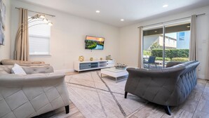 Una sala de estar moderna con un sofá, un sillón, una mesa de centro, un televisor de pantalla plana y un ventanal corredero que da a un espacio exterior.