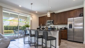 Una cocina moderna con una isla central, taburetes de bar, electrodomésticos de acero inoxidable y una puerta corrediza de vidrio que da a un patio.