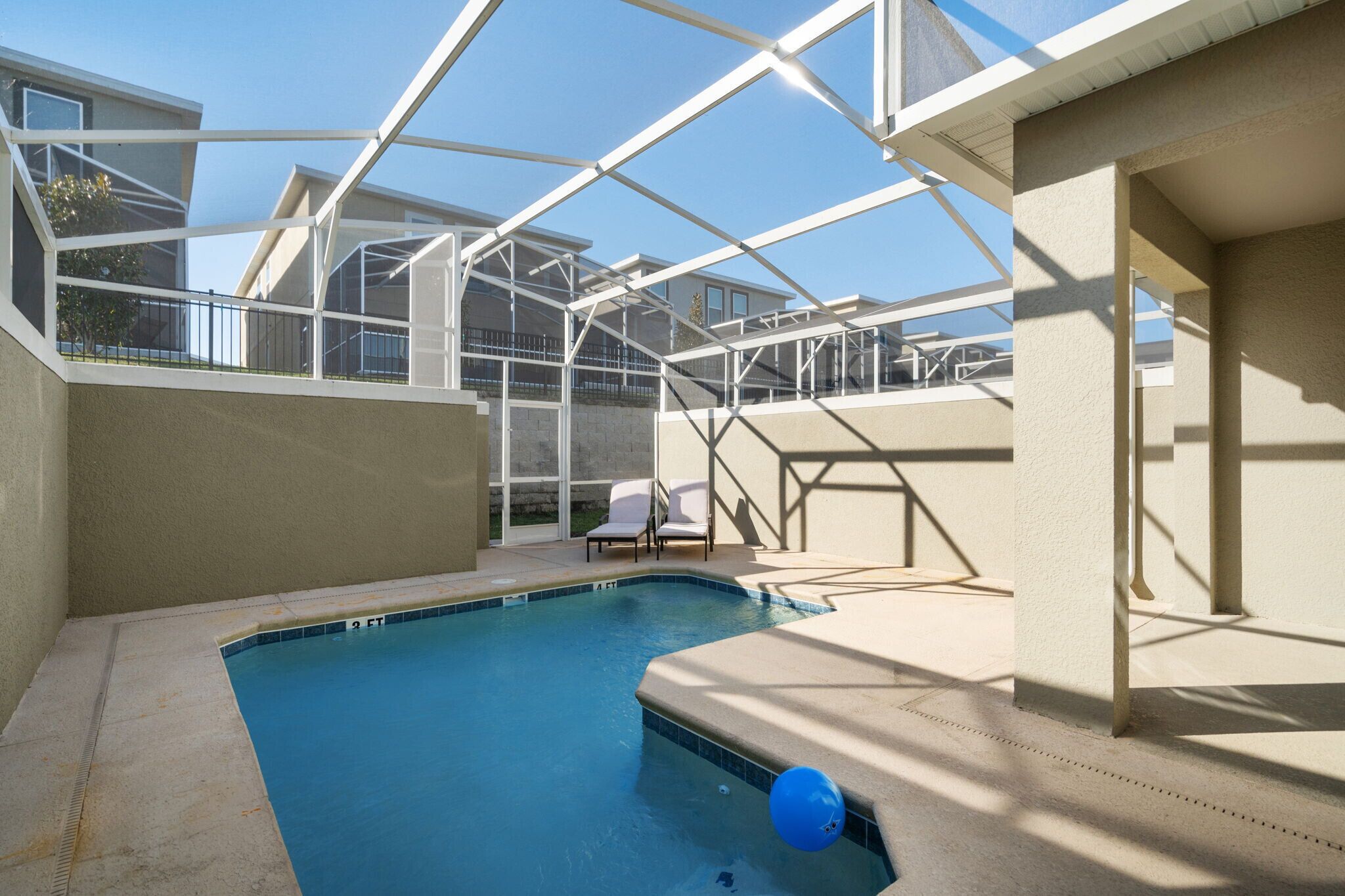 A swimming pool with a glass enclosure, a chair, and a view of neighboring buildings.