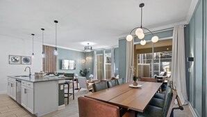 Een moderne keuken met een centraal eiland, een eethoek met een lange tafel en banken, en een zithoek met een bank en televisie.