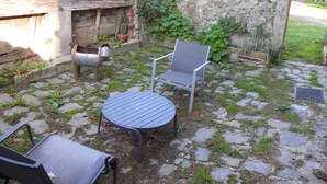 Eine Terrasse mit einem Metalltisch und zwei Stühlen, einer Steinmauer und einer Kakteenpflanze.