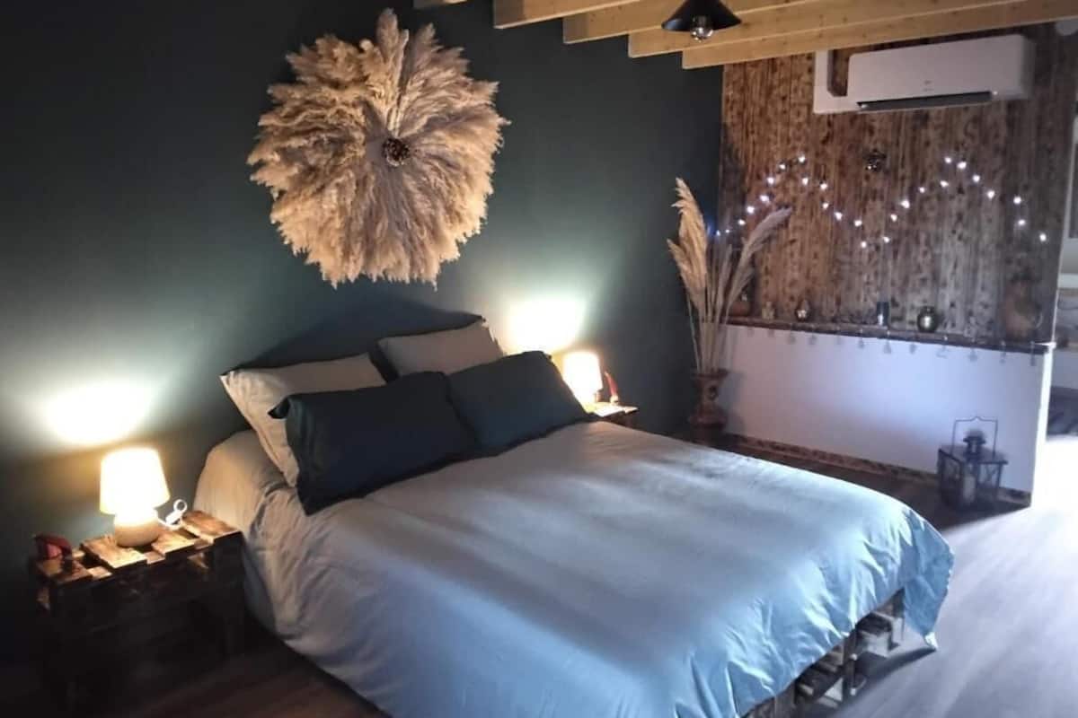 A bedroom with a bed, bedside lamps, a decorative wall piece, and a wall-mounted air conditioner.