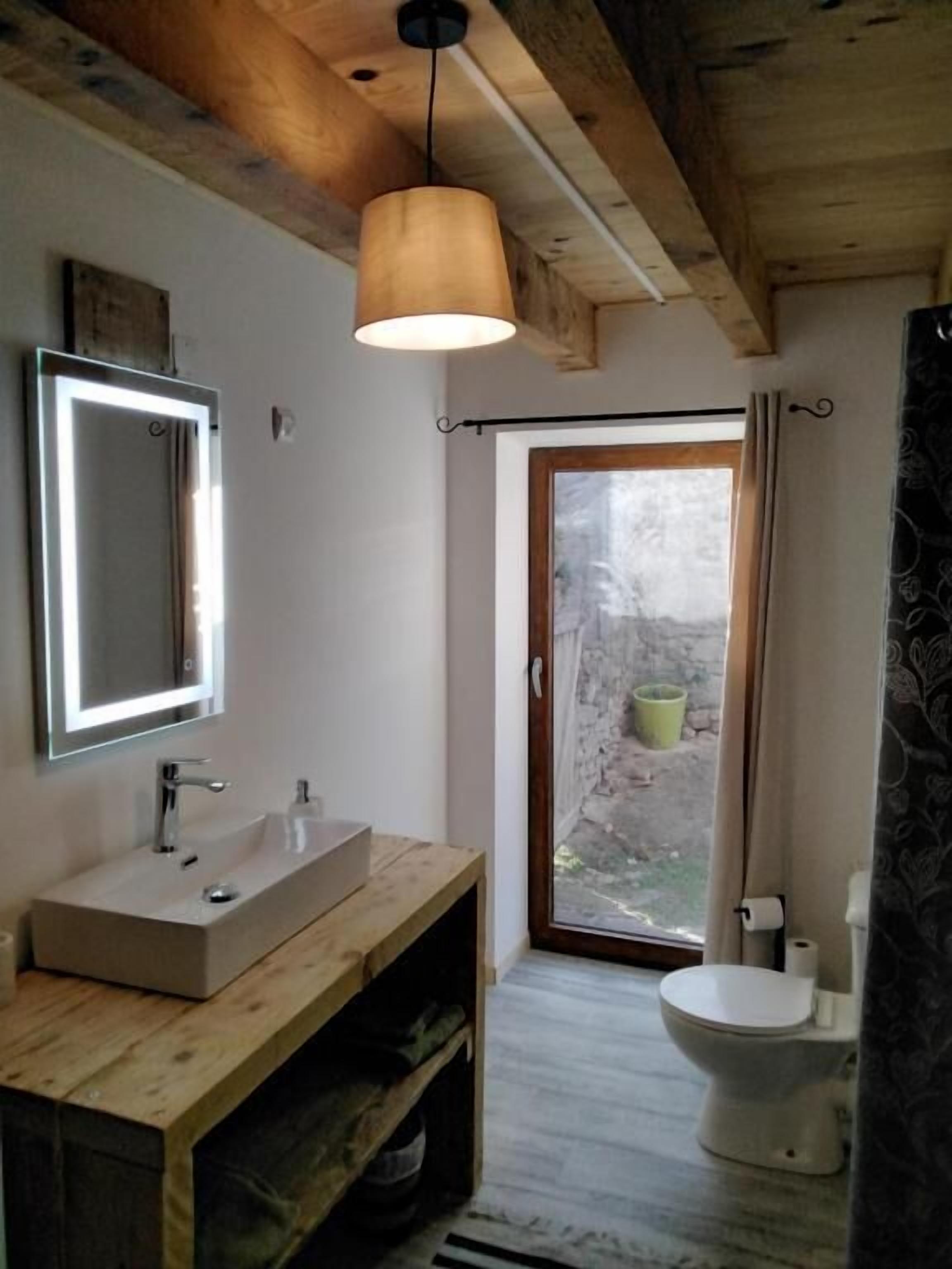 A modern bathroom with a wooden vanity, a large mirror, and a hanging light fixture.