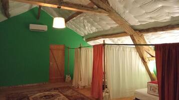 Ein Zimmer mit grüner Wand, Holzbalken, einem Bett mit rotem Kissen und einer hängenden Leuchte.