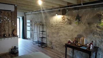 A rustic room with exposed wooden beams, a stone wall, a bed, a table with various items, and a ladder against the wall.