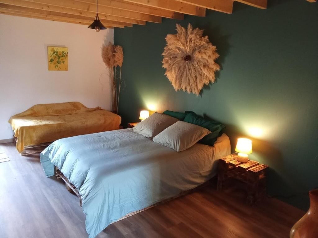 A bedroom with two beds, wooden flooring, a green accent wall, and a decorative wall hanging.