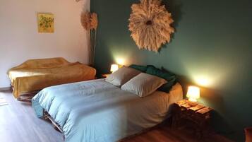 A bedroom with two beds, wooden flooring, a green accent wall, and a decorative wall hanging.