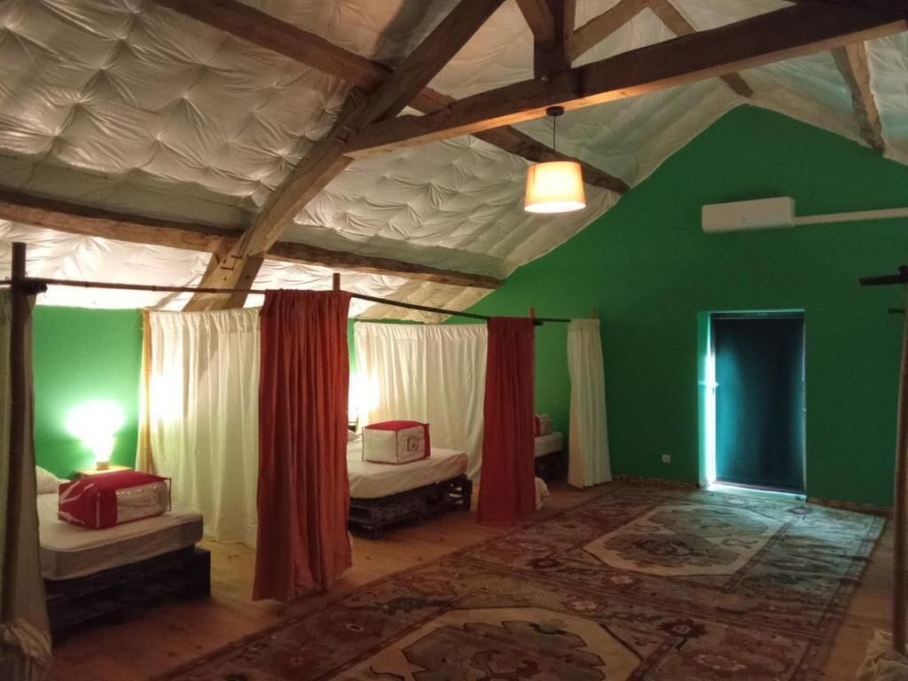 Een kamer met een hoge plafond, een bed met een rode deken, een klein tafeltje en een kamerbreed tapijt met een patroon.