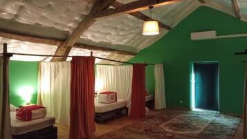 Een kamer met een hoge plafond, een bed met een rode deken, een klein tafeltje en een kamerbreed tapijt met een patroon.
